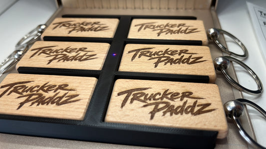 Set of wooden keychains with 'Trucker Paddz' branding in a display case.